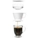 An OXO pour over coffee dripper with a clear water tank being poured into a glass cup of brown coffee.