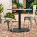 A Lancaster Table & Seating Excalibur black outdoor table base on a brick patio with chairs.