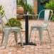 A black Lancaster Table & Seating Excalibur outdoor table base with a black pole on a table with two chairs on a brick patio.