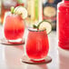 A glass of Finest Call Prickly Pear Syrup with a red drink and lime wedge.