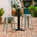 A Lancaster Table & Seating outdoor table with a black pole and stools on a brick patio.