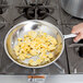 A hand using a Vollrath stainless steel fry pan to cook scrambled eggs on a stove.