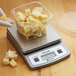 A gloved hand weighing cheese on a San Jamar kitchen scale.