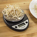 A plate of noodles being weighed on a black digital portion scale.