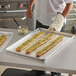 A person wearing a white shirt and black striped pants holds a Vollrath bun / sheet pan with long bread loaves on it.