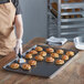 A person using a pastry spatula to place pastries on a Vollrath non-stick sheet pan.