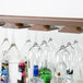 An American Metalcraft walnut hanging bar glass rack holding wine and martini glasses and a bottle of liquor.