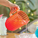 A hand pouring red liquid into a Choice coral plastic beverage pitcher.