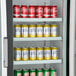 An Avantco black swing glass door merchandiser refrigerator full of cans of soda.