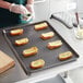 A person putting a piece of bread with cheese and herbs on a Vollrath non-stick sheet pan.