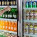 A hand reaching for a beverage in an Avantco merchandising refrigerator with a customizable panel.