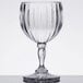 A clear GET SAN plastic wine glass with a fluted design and curved stem on a table.