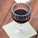 A customizable fluted SAN plastic wine glass filled with red wine on a table.