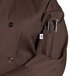 A brown Uncommon Chef Orleans long sleeve chef coat with pockets and buttons.