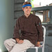 A man sitting on a stool wearing an Uncommon Chef long sleeve chef coat.
