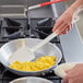 A hand using a Vollrath SoftSpoon to stir scrambled eggs in a pan.