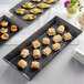 An American Metalcraft black faux slate rectangular melamine platter of appetizers on a table.