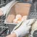 A person in gloves holding a stainless steel pan of shrimp over a steam table.