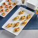 A white rectangular melamine platter of appetizers with asparagus and cheese on a table.