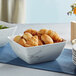 A white marble square melamine bowl filled with croissants and bread on a table.