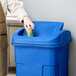 A person in an apron putting a cup into a blue Toter trash can.