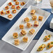 An American Metalcraft white marble rectangular melamine platter with a variety of appetizers on a table.
