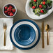 A table setting with a blue plate, salad, and American Metalcraft Jane Casual denim melamine bowl filled with strawberries.