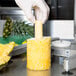 A person in a white glove using a Nemco pineapple corer to peel a pineapple.