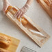 A person wearing gloves in a bakery putting a loaf of bread in a Bagcraft Packaging paper bag.