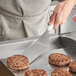 A person using a Vollrath stainless steel hamburger turner with a white handle to cook meat patties.