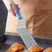 A person using a Dexter-Russell blue perforated turner to lift cooked salmon off a grill.