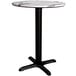 A Lancaster Table & Seating round dining table with a white marble top and black cross base.