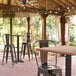 A Lancaster Table & Seating bar height table with a textured Yukon Oak finish and cross base plate on a covered patio.