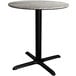 A Lancaster Table & Seating round dining table with a textured concrete surface and black cross base.