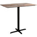 A Lancaster Table & Seating rectangular bar height table with a textured wood plank top and black cross base.