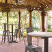 A Lancaster Table & Seating bar height table with a textured mixed plank finish and cross base plate on a brick patio.