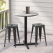 A Lancaster Table & Seating round counter height table with a cross base plate on an outdoor patio with two black stools.