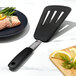 A black OXO silicone slotted spatula turning fish on a plate.