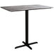 A Lancaster Table & Seating rectangular bar height table with a black metal cross base plate and textured gray top.