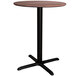 A Lancaster Table & Seating round counter height table with a textured walnut top and black cross base.