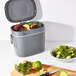 An OXO charcoal grey rectangular compost bin on a counter with a bowl of salad and a lime.
