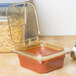 A Carlisle amber plastic food pan filled with pasta and sauce on a kitchen counter.