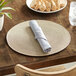 A RITZ taupe round polypropylene placemat on a wood table with food and a glass of water.