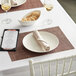 A brown, black, and silver RITZ® basketweave placemat on a white table with a place setting.