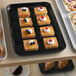 A black Cambro market tray of pastries on a table.