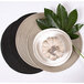A RITZ black round polypropylene placemat with a plate and a leaf on it.