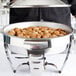 A person holding a Vollrath stainless steel food pan on a table with cookies and nuts.