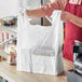 A person holding a Choice white heavy-duty large T-shirt bag full of groceries.