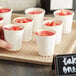 A hand holding a tray of Choice white paper cold cups filled with strawberry juice.