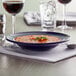 A Tuxton Concentrix cobalt bowl of soup on a napkin next to a glass of wine.